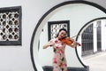 Beautiful Asian Chinese woman in traditional chi-pao cheongsam play violin in in a garden stand under arched door Royalty Free Stock Photo