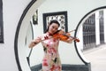 Beautiful Asian Chinese woman in traditional chi-pao cheongsam play violin in in a garden stand under arched door Royalty Free Stock Photo