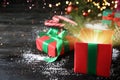 Beautiful Christmas gift box with magic light on black wooden table Royalty Free Stock Photo