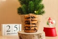 Beautiful Christmas postcard with chocolate cookies on wooden stand, snowball, Christmas tree, and calendar dated December 25.