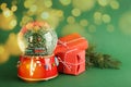 Beautiful Christmas snow globe, gift boxes and fir tree branch on green background, bokeh effect. Space for text Royalty Free Stock Photo