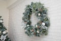 Beautiful Christmas wreath of fir branches, cones, white baubles, flowers, berries and icycles on brick wall with garland lights.