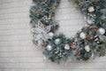 Beautiful Christmas wreath of fir branches, cones, white baubles, flowers, berries and icycles on brick wall with garland lights.