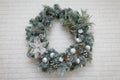 Beautiful Christmas wreath of fir branches, cones, white baubles, flowers, berries and icycles on brick wall with garland lights.