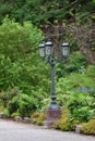 Beautiful classic iron lamppost of three lamps near the sidewalk against the background of bushes and trees in a European city