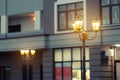 Beautiful classic metal street lamp in evening against modern building in evening. Warm light iron retro lantern at city Royalty Free Stock Photo