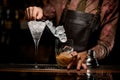 beautiful clear martini glass full of ice and glass of shaker with cocktail in which pouring ice cubes are on bar Royalty Free Stock Photo