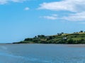 Beautiful clear sky over a calm water surface on a summer day. The picturesque green coast of Ireland. Several buildings on the