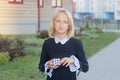 Beautiful and clever blonde kid girl solves a cube puzzle, outside near school.