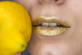 Beautiful closeup with female lips with gold color makeup and lemon. Glitter cosmetics