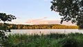 A beautiful cloudy sky at sunset over the lake. The branches of an alder tree lean over the reeds in the water. On the far shore s Royalty Free Stock Photo