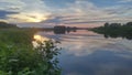 A beautiful cloudy sky at sunset over the river. The high bank of the river is overgrown with grass and alder. The opposite bank o Royalty Free Stock Photo