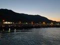 Beautiful coast and beach with outlines of mountains against the backdrop of sunset from the sea or ocean and burning lights of Royalty Free Stock Photo