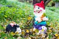 Beautiful and colorful garden gnome with a little hedgehog are standing under a tree. Yellowing leaves from the tree.
