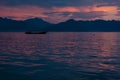 Beautiful colorful purple sunset on calm sea with pink, orange glare on smooth waves, silhouette fishing boat and dark blue. Royalty Free Stock Photo