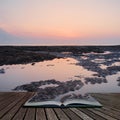 Beautiful colorful sunrise reflected in rock pools at low tide on beach coming out of pages of open story book Royalty Free Stock Photo