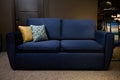 Beautiful comfortable minimalist stylish navy blue sofa with yellow and patterned cushion in the furniture store exposition center