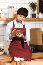 Beautiful concentrated barista in apron writing in notebook.