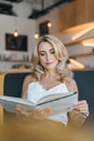 beautiful concentrated blonde woman reading book while sitting