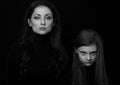 Beautiful concentrated serious mother and her angry emotional thinking daughter looking on black shadow background. Concept family