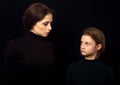 Beautiful concentrated serious mother and her angry emotional thinking daughter looking each other on black shadow background.