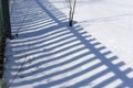 Beautiful contrasting blue shadow of a wooden rustic fence on the white snow on a sunny winter day. Background. Abstract Royalty Free Stock Photo