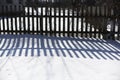 Beautiful contrasting blue shadow of a wooden rustic fence on the white snow on a sunny winter day. Background. Abstract Royalty Free Stock Photo