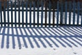 Beautiful contrasting blue shadow of a wooden rustic fence on the white snow on a sunny winter day. Background. Abstract Royalty Free Stock Photo