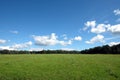 Beautiful countryside landscape with wide green field and deciduous forest at far under white clouds on blue sky in the summer day Royalty Free Stock Photo