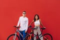 Beautiful couple of cyclists in casual clothes stand on a red background with bicycles and pose for the camera. Stylish parasport Royalty Free Stock Photo