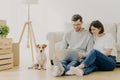 Beautiful couple with dog sit on floor in spacious living room, make purchasing online, buy furniture for new home, have to unpack Royalty Free Stock Photo