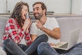 Beautiful couple is doing shopping online using a laptop and smiling while sitting on couch at home, woman is holding a Royalty Free Stock Photo