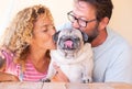 Beautiful couple embracing and kissing their old pug dog. Lovely family and best friends concept