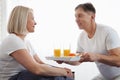 Beautiful couple having breakfast lying in bed at home. Handsome man and attractive woman are enjoying spending time Royalty Free Stock Photo