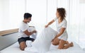 Beautiful couple having fun by fighting with a pillow on bed after waking up in bright bedroom Royalty Free Stock Photo