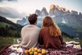 Beautiful couple having a picnic in flowering alpine meadow and admiring a scenic view from a mountain top. Young man and young