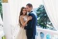 Beautiful couple honeymoon embracing each other and standing on a white balcony. Young groom in a black suit and a Royalty Free Stock Photo