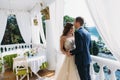 Beautiful couple honeymoon embracing each other and standing on a white balcony. Young groom in a black suit and a Royalty Free Stock Photo