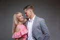 Beautiful couple is looking at each other and smiling while standing straight on gray background.
