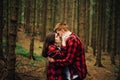 A beautiful couple in love in red shirts passionately kissing in a coniferous forest among the trunks of trees. Love story photo Royalty Free Stock Photo