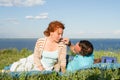 beautiful couple lying on the lawn in summer grass on the river bank. Water, sky and clouds for couple