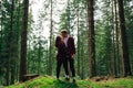 Beautiful couple man and woman in red shirts stand in a beautiful mountain forest and kissing holding hands on a background of Royalty Free Stock Photo