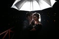 Beautiful couple man with woman with white umbrella in flash lights and rain drops