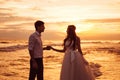 A beautiful couple of newlyweds, the bride and groom walking on the beach. Gorgeous sunset and sky. Wedding dresses, a Royalty Free Stock Photo