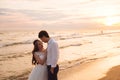 A beautiful couple of newlyweds, the bride and groom walking on the beach. Gorgeous sunset and sky. Wedding dresses, a Royalty Free Stock Photo