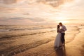 A beautiful couple of newlyweds, the bride and groom walking on the beach. Gorgeous sunset and sky. Wedding dresses, a Royalty Free Stock Photo