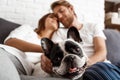 Beautiful couple resting on sofa with dog. Focus pug.