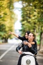 Beautiful happy couple riding scooter and having fun, woman pointed with hands and smiling. Royalty Free Stock Photo