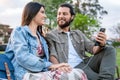 Couple sharing music and using mobile in bench park Royalty Free Stock Photo