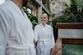 Beautiful couple in spa robes standing in hotel greenhouse, looking at each another, enjoying romantic wellness